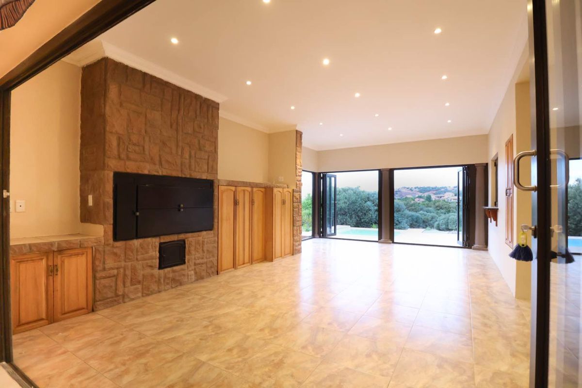 Spacious living area featuring a stone-clad built-in fireplace, custom cabinetry, and large stacking doors opening to an outdoor pool area.