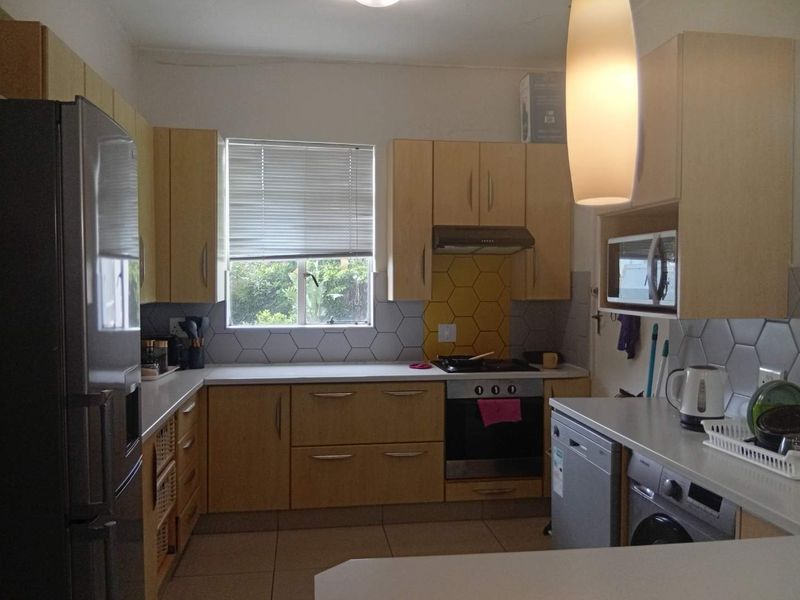 A functional kitchen featuring light wood cabinetry, a hexagonal tiled splashback, built-in oven with extractor fan, and integrated microwave space.