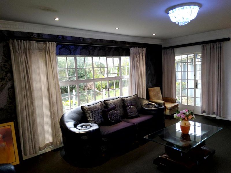 Spacious living room featuring large windows, french doors, crown molding, and elegant lighting fixtures, offering a bright and comfortable atmosphere.