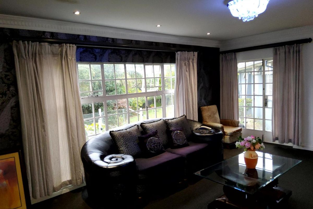 Spacious living room featuring large windows, french doors, crown molding, and elegant lighting fixtures, offering a bright and comfortable atmosphere.