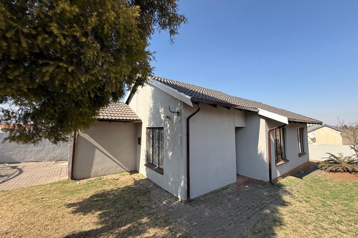 Rear view of the house featuring a tiled roof, paved walkway, and established garden area.
