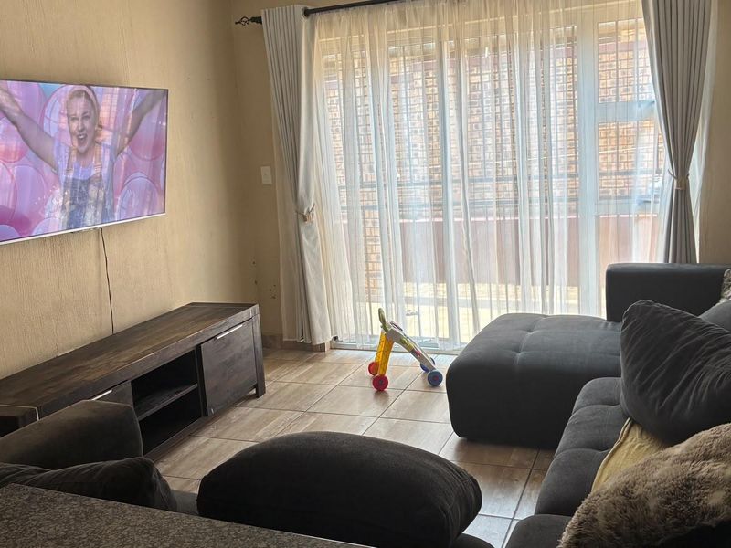 A living room featuring tiled flooring and a sliding glass door providing access to the exterior, with wall-mounted television space.