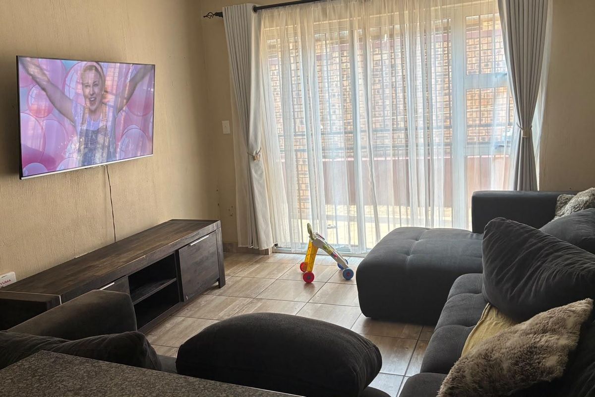 A living room featuring tiled flooring and a sliding glass door providing access to the exterior, with wall-mounted television space.