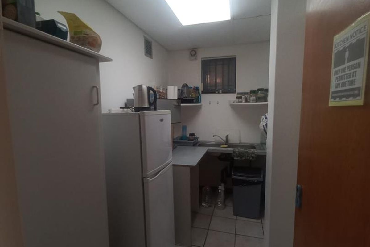 A compact office kitchenette featuring basic cabinetry, a stainless steel sink, and tiled flooring, providing essential utility space for staff.