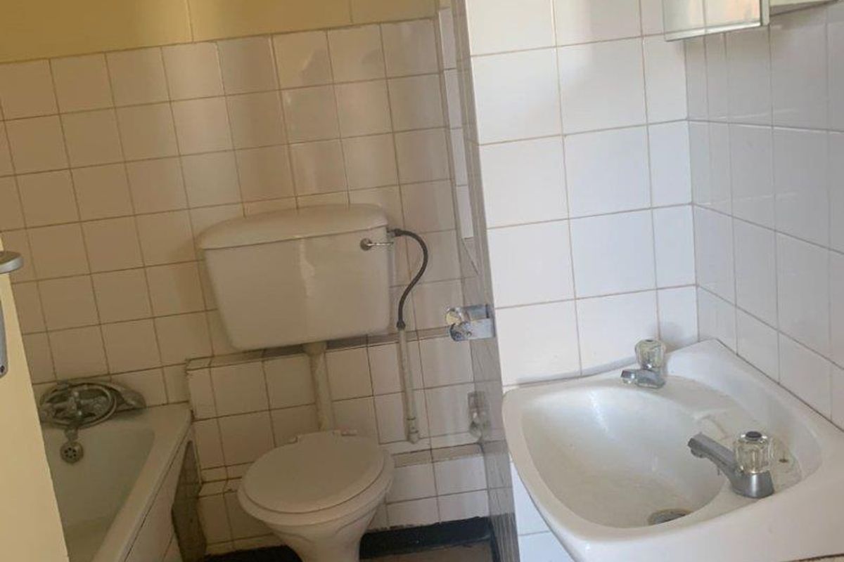 A compact, dated bathroom featuring a standard bathtub, pedestal sink, and toilet with white wall tiling and original fixtures.