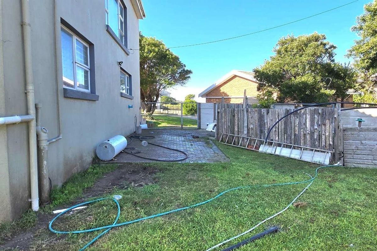 Rear exterior view of the property featuring a paved area, lawn, and timber boundary fencing with an integrated water storage tank.