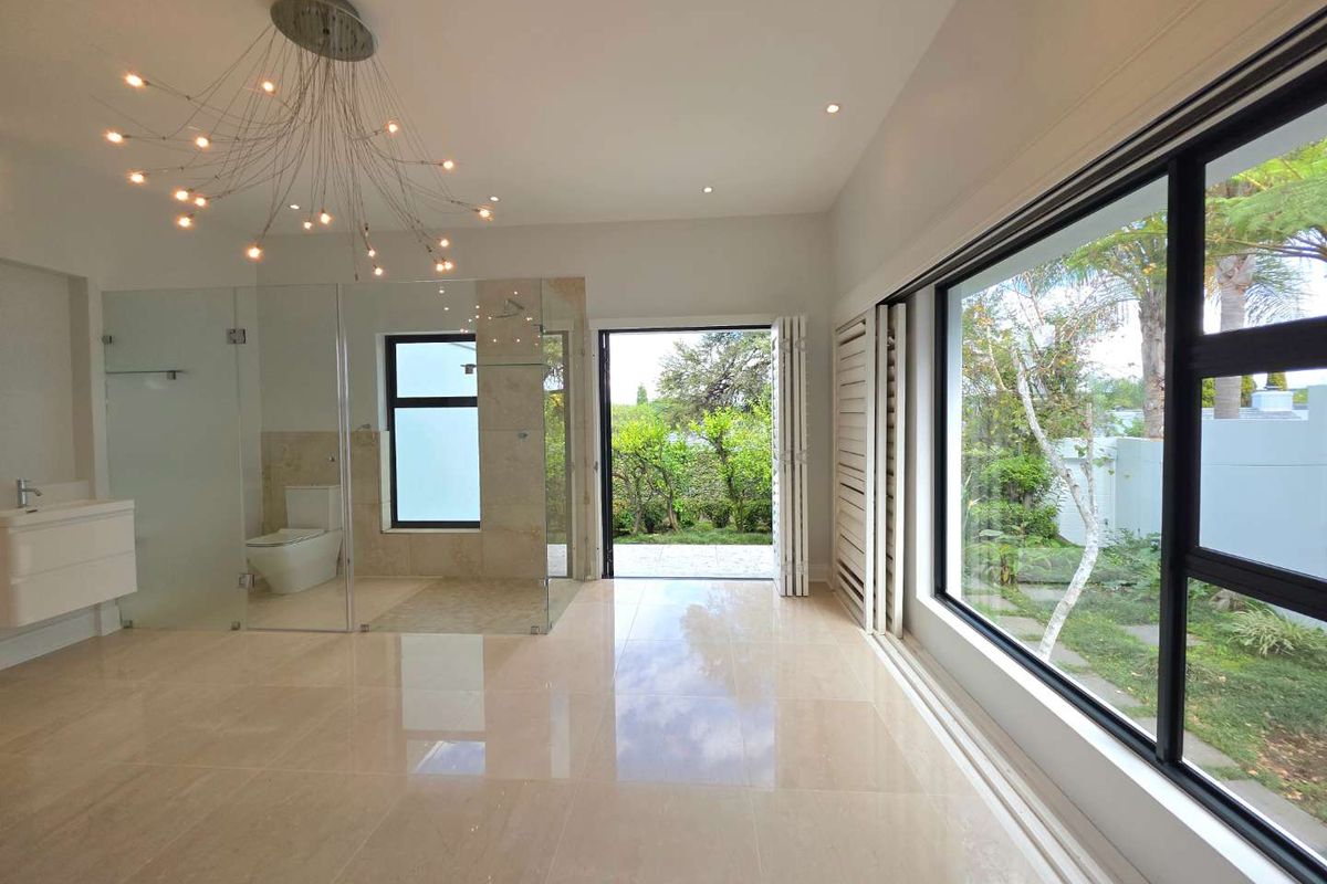 Spacious modern bathroom featuring large format floor tiles, a glass-enclosed shower, wall-mounted vanity, and expansive windows with direct garden access.