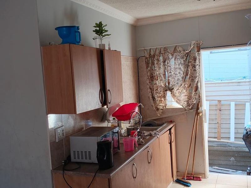 A compact kitchen featuring laminate cabinetry, tiled flooring, and direct access to an outdoor area, requiring cosmetic updates to improve its overall condition.