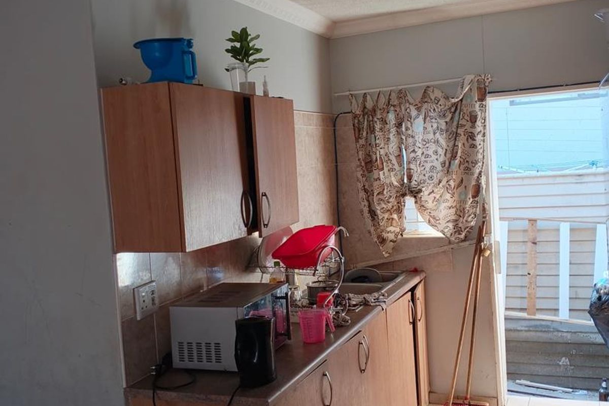 A compact kitchen featuring laminate cabinetry, tiled flooring, and direct access to an outdoor area, requiring cosmetic updates to improve its overall condition.