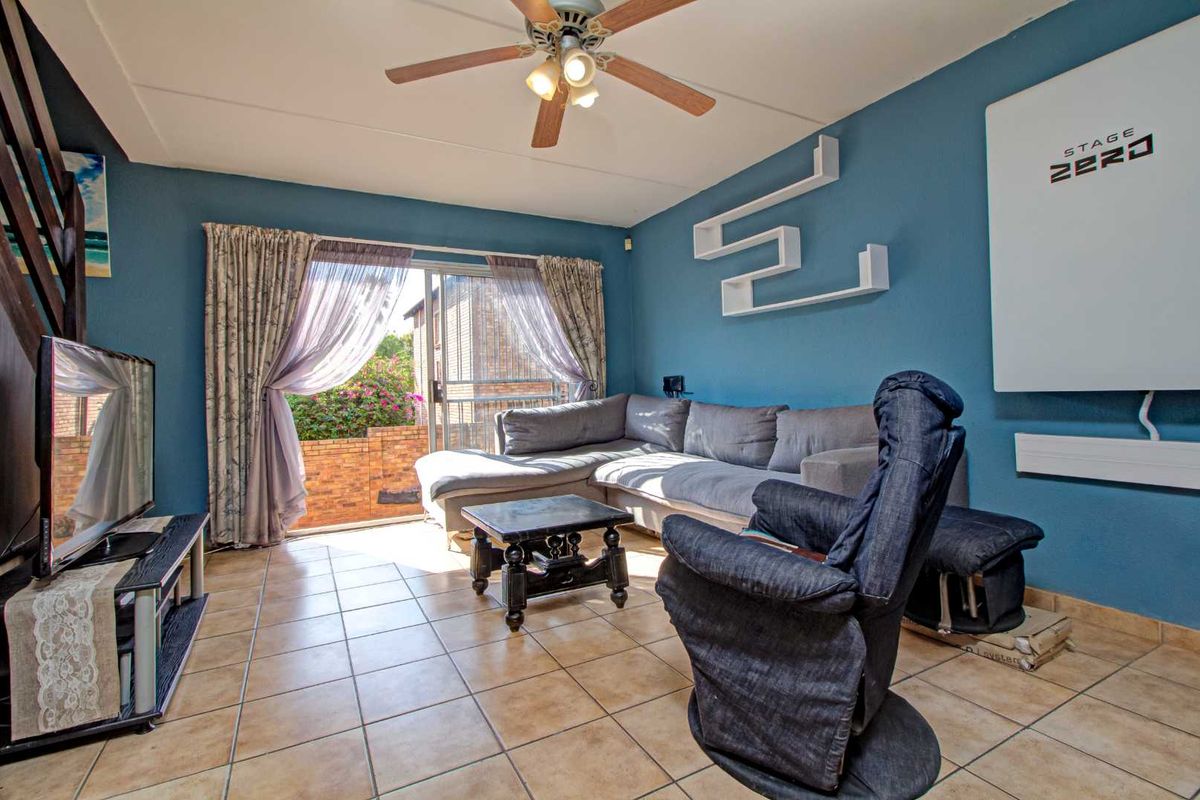 A living room featuring tiled flooring, a ceiling fan, and sliding glass doors that open to an outdoor patio area.