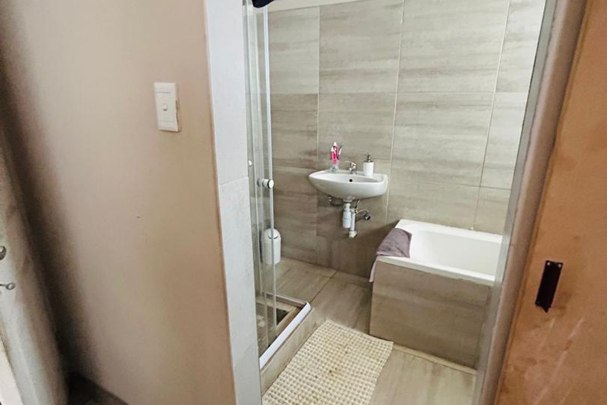 A functional bathroom featuring a shower enclosure, wall-mounted basin, and a built-in bathtub with neutral tiled finishes throughout.