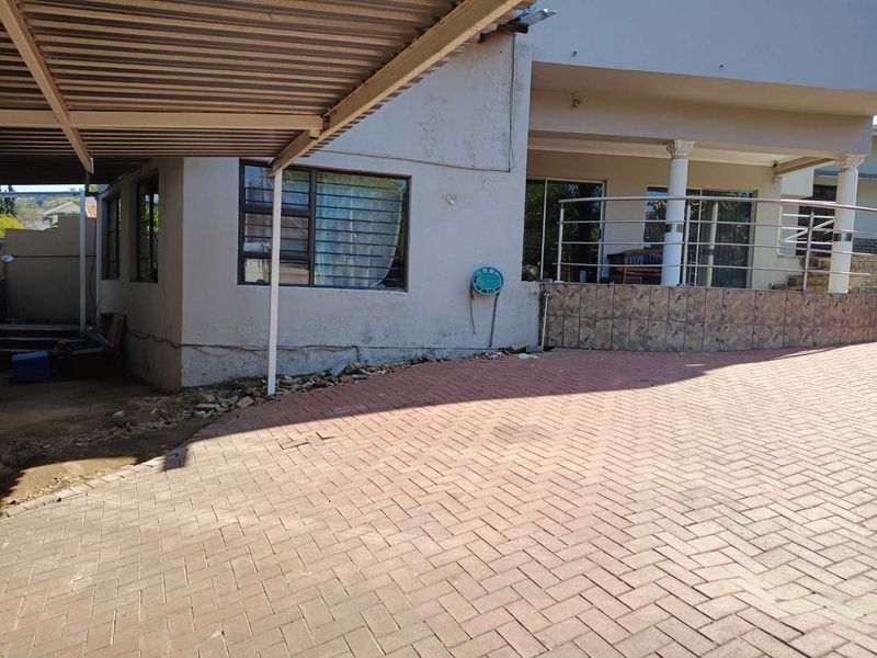 Front exterior view featuring a paved driveway, covered carport, and a raised patio area with stainless steel balustrades and sliding door access.