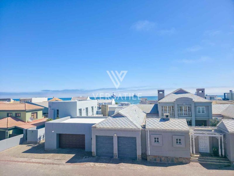 Aerial view of the property showcasing the exterior facade, double garage, paved driveway, and surrounding coastal neighborhood.