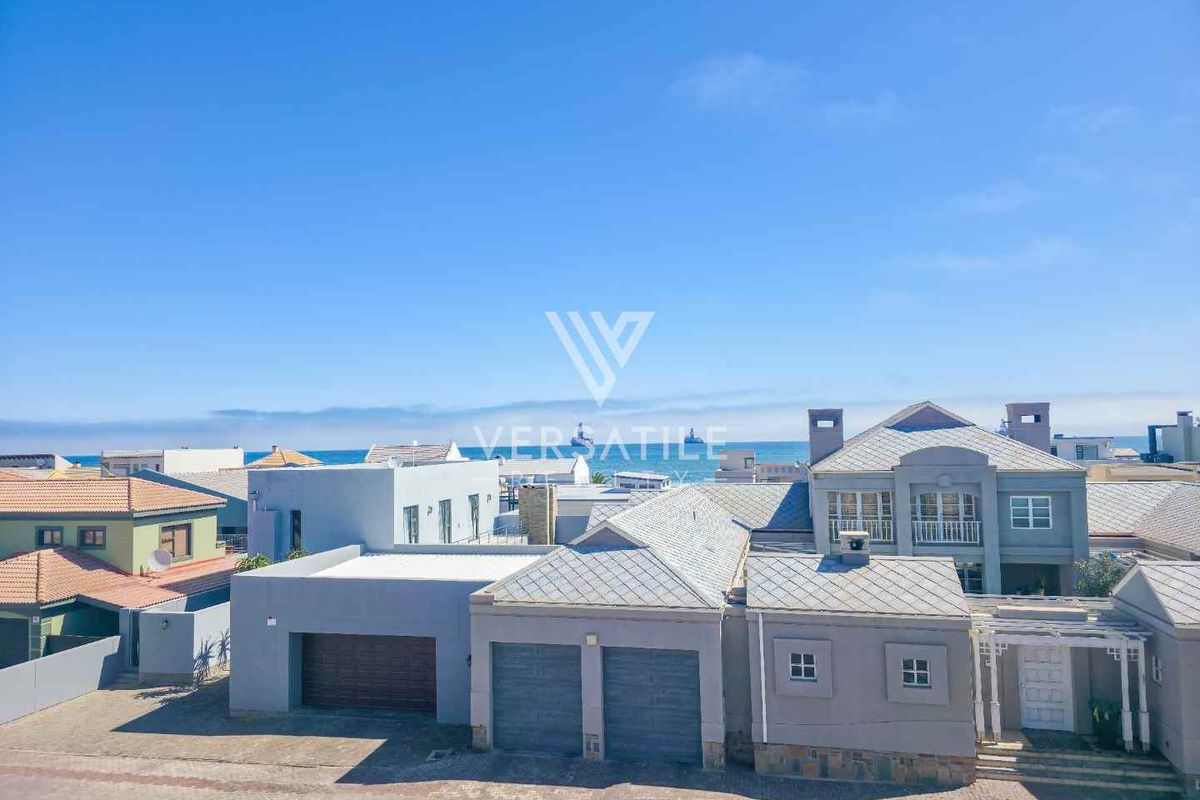 Aerial view of the property showcasing the exterior facade, double garage, paved driveway, and surrounding coastal neighborhood.