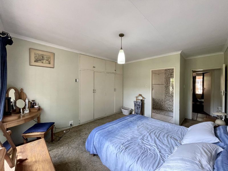 A functional bedroom featuring built-in cupboards, carpeted flooring, and direct access to an en-suite bathroom with mosaic tile finishes.