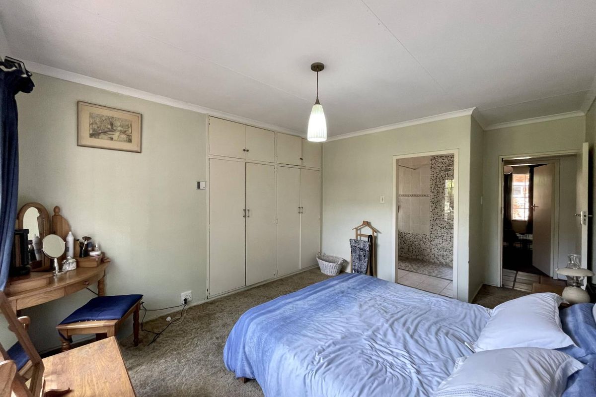 A functional bedroom featuring built-in cupboards, carpeted flooring, and direct access to an en-suite bathroom with mosaic tile finishes.