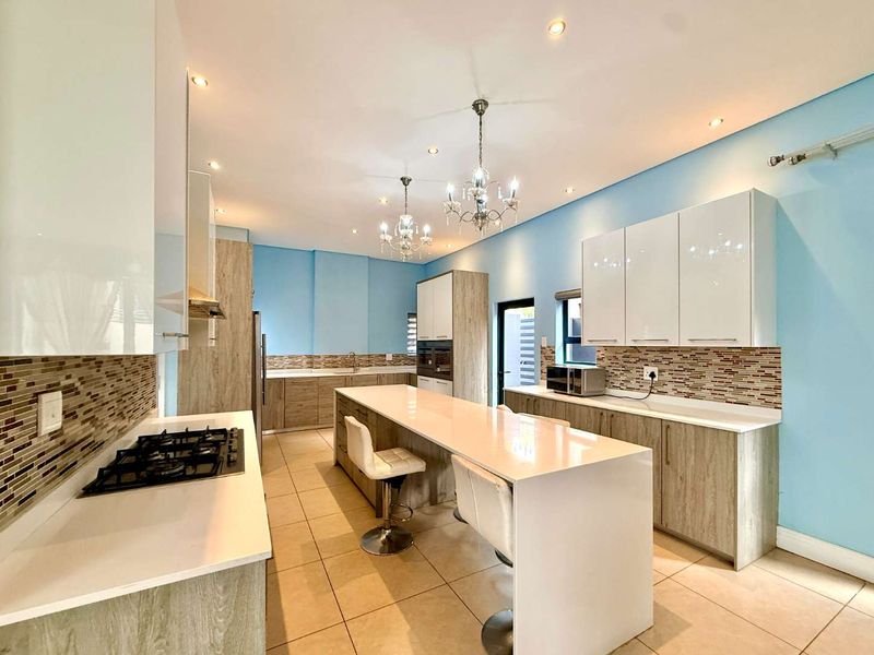 Modern kitchen featuring a central island with stone countertops, gas hob, built-in oven, and contemporary cabinetry with a mosaic tile backsplash.