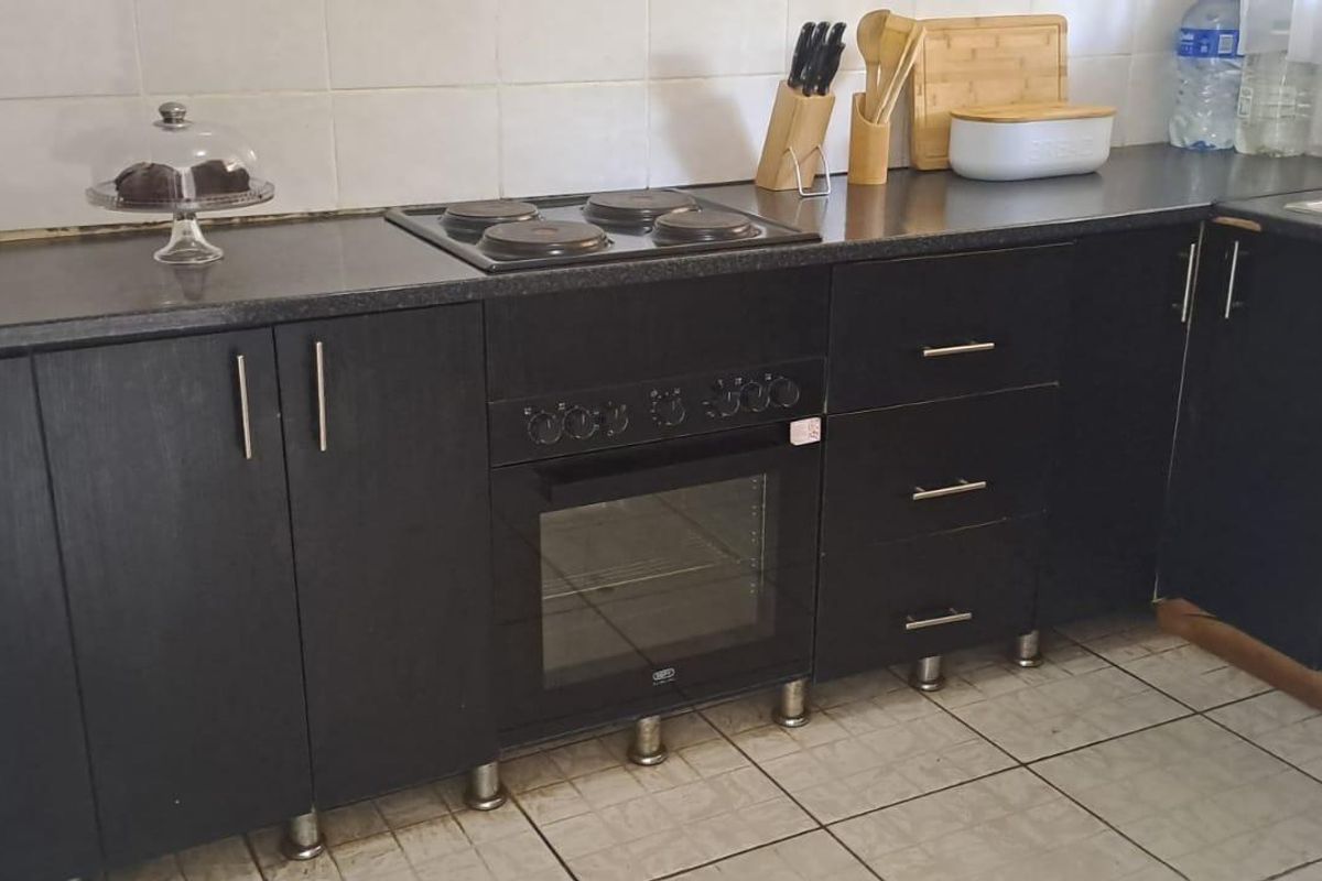 Compact kitchen featuring dark laminate cabinetry, built-in oven, electric hob, tiled splashback, and a stainless steel sink.