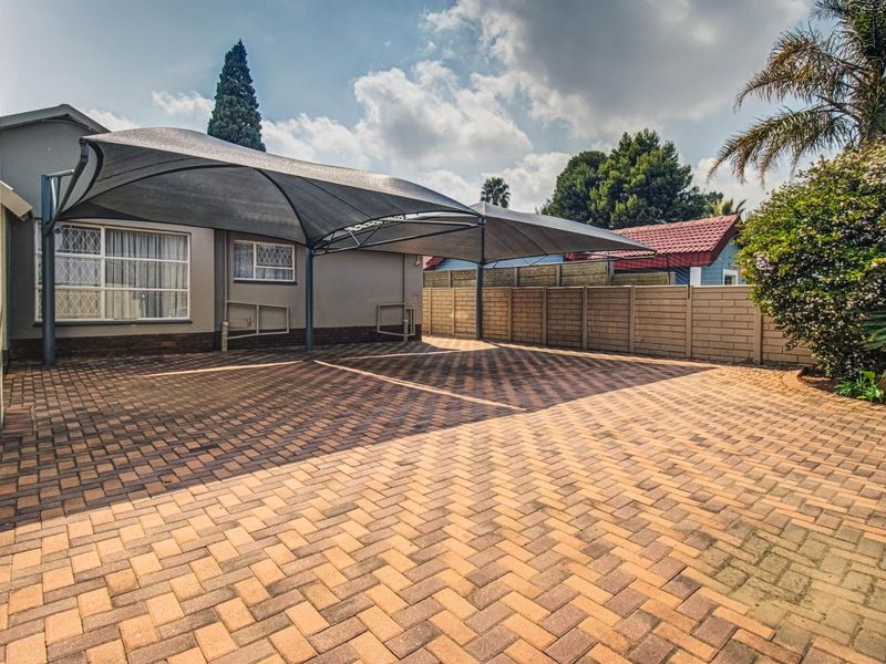 A well-maintained paved driveway featuring a modern shade sail carport and secure perimeter walling, providing ample off-street parking space.