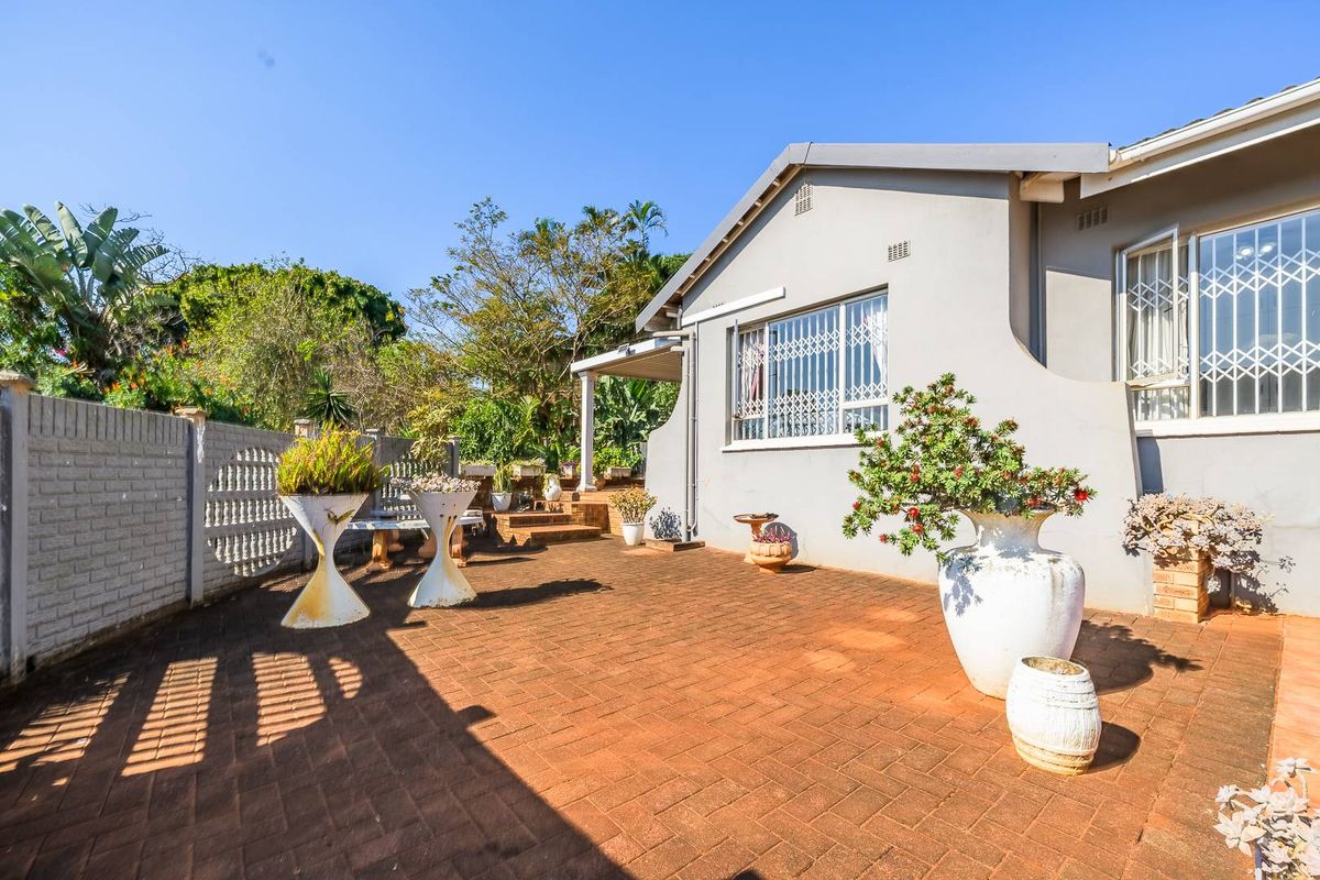 A well-maintained rear exterior featuring a spacious paved patio area, covered veranda, and secure boundary walling.