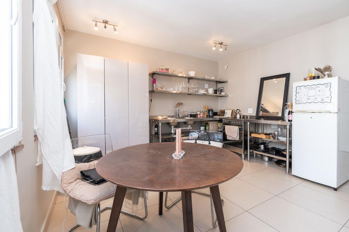 A functional kitchen area featuring stainless steel work surfaces, open shelving, a freestanding stove, and neutral tiled flooring.