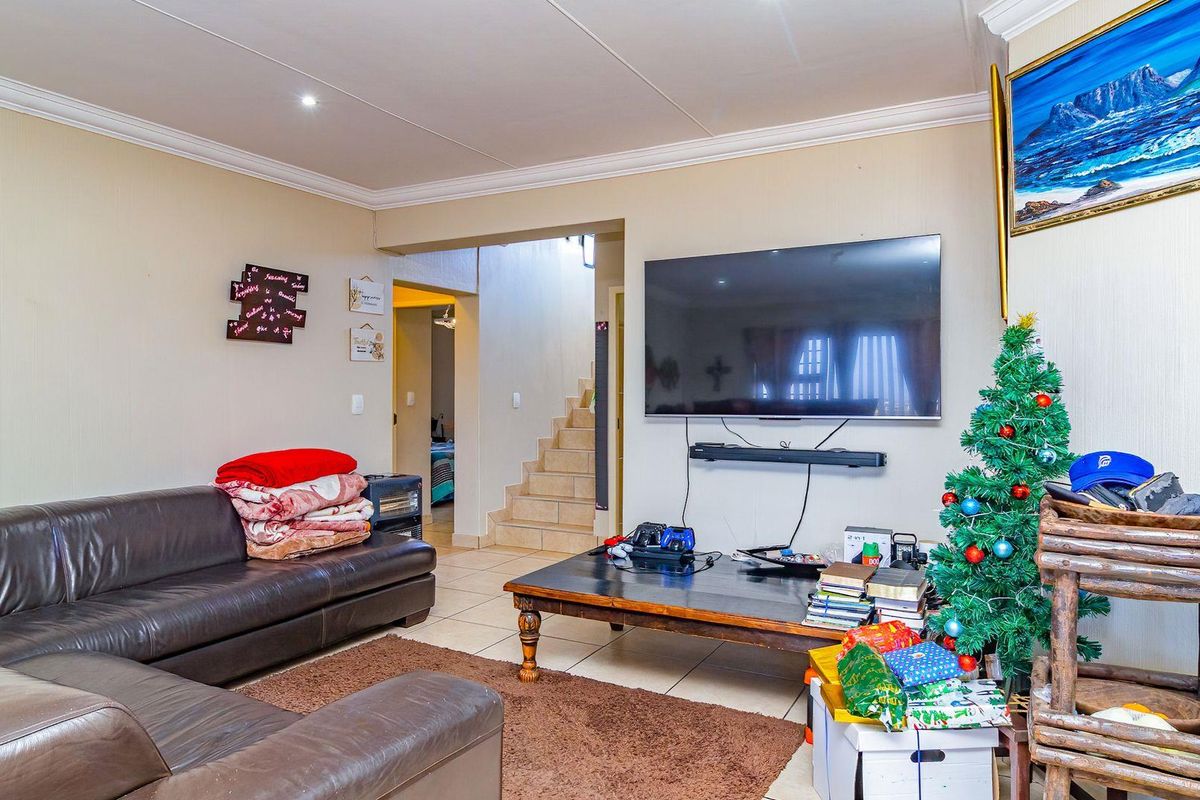 A living room featuring tiled flooring, crown molding, and a wall-mounted television, with an adjacent staircase leading to the upper level.