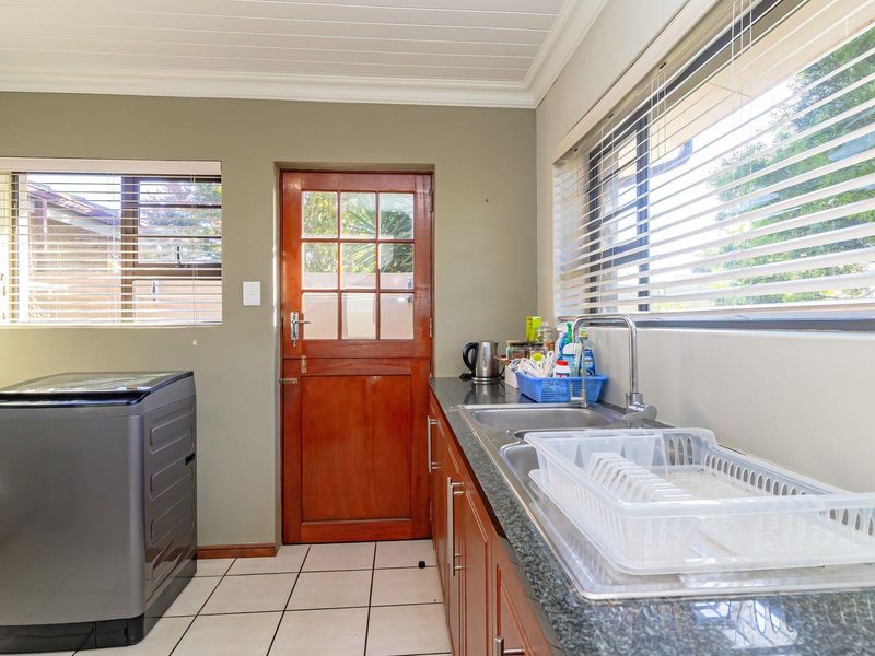 A functional laundry room featuring built-in cabinetry, a stainless steel sink with granite countertops, tiled flooring, and direct access to the exterior.