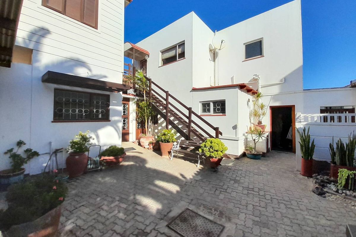 A paved rear courtyard area featuring a timber staircase leading to an upper level, surrounded by white exterior walls and established potted greenery.