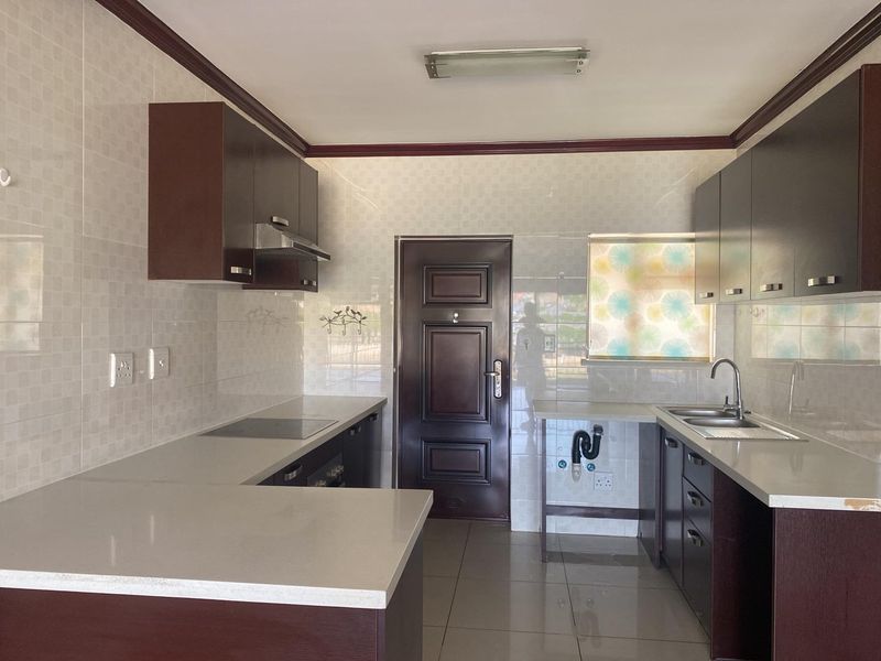 A functional kitchen featuring dark cabinetry, stone-look countertops, tiled walls, a built-in hob, and a double-basin sink with plumbing for an appliance.