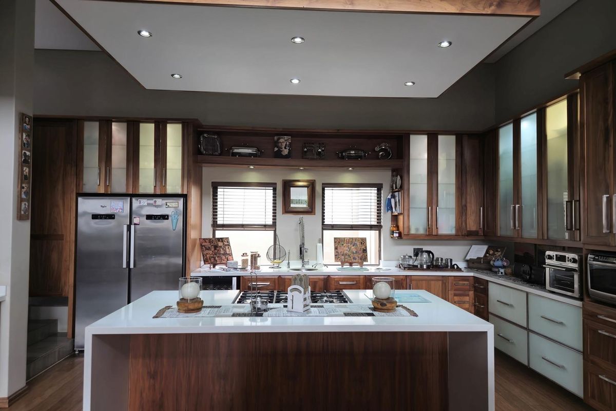 A well-appointed kitchen featuring dark wood cabinetry, a central island with a gas hob, integrated appliances, and modern recessed lighting.