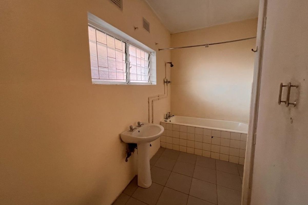 A dated bathroom featuring a pedestal basin, bathtub with shower head, and tiled flooring, requiring cosmetic updates to modernize the space.