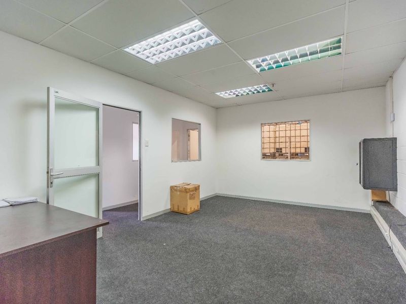 A functional office space featuring carpeted flooring, suspended ceiling with recessed lighting, and an internal window with security grille.