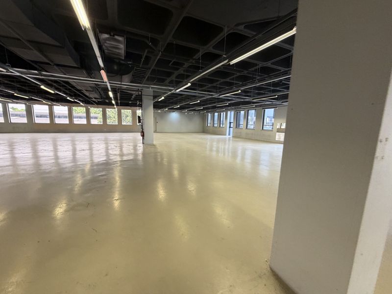 Spacious open-plan industrial office area featuring polished epoxy flooring, exposed waffle slab ceilings, and abundant natural light from large perimeter windows.