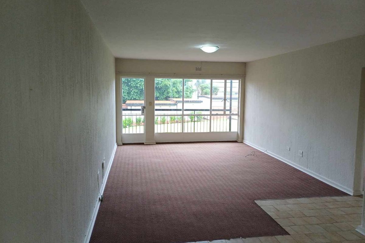 An empty, spacious living area featuring large glass doors, carpeted flooring, and a tiled entrance section, offering a blank canvas for interior design.
