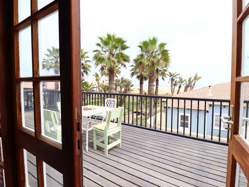 A wooden balcony featuring a metal balustrade, accessible through classic timber french doors, offering an outdoor space with coastal views.