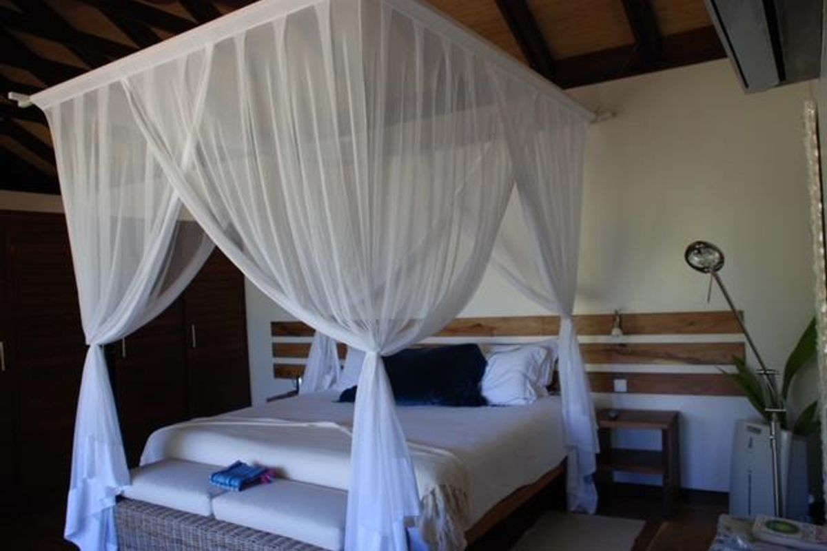 A well-maintained bedroom featuring exposed timber ceiling beams, built-in wooden wardrobe cabinetry, and a decorative timber wall panel behind the bed area.
