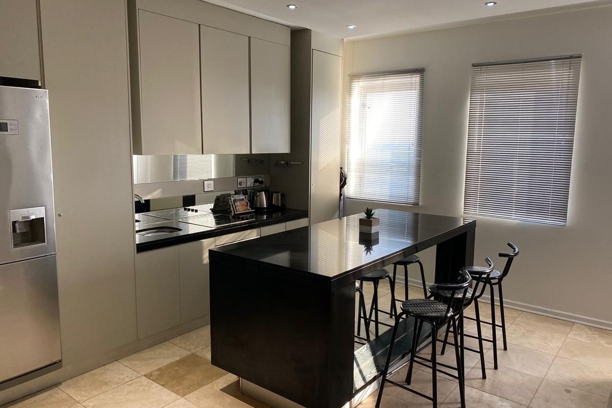 Modern kitchen featuring sleek cabinetry, a black stone island countertop, integrated appliances, and tiled flooring with natural light from dual windows.