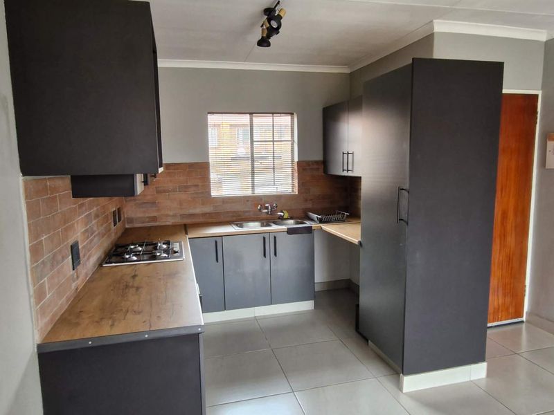 A modern kitchen featuring dark cabinetry, wood-look laminate countertops, a gas hob, and a brick-style tiled backsplash with neutral floor tiles.