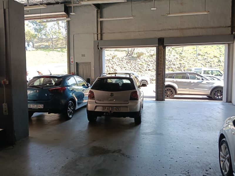 Spacious industrial garage area featuring concrete flooring, high ceilings with fluorescent lighting, and large roller shutter doors for vehicle access.
