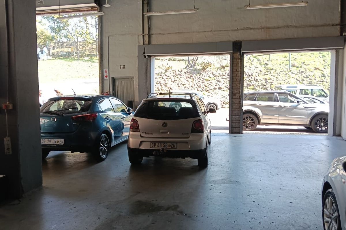 Spacious industrial garage area featuring concrete flooring, high ceilings with fluorescent lighting, and large roller shutter doors for vehicle access.