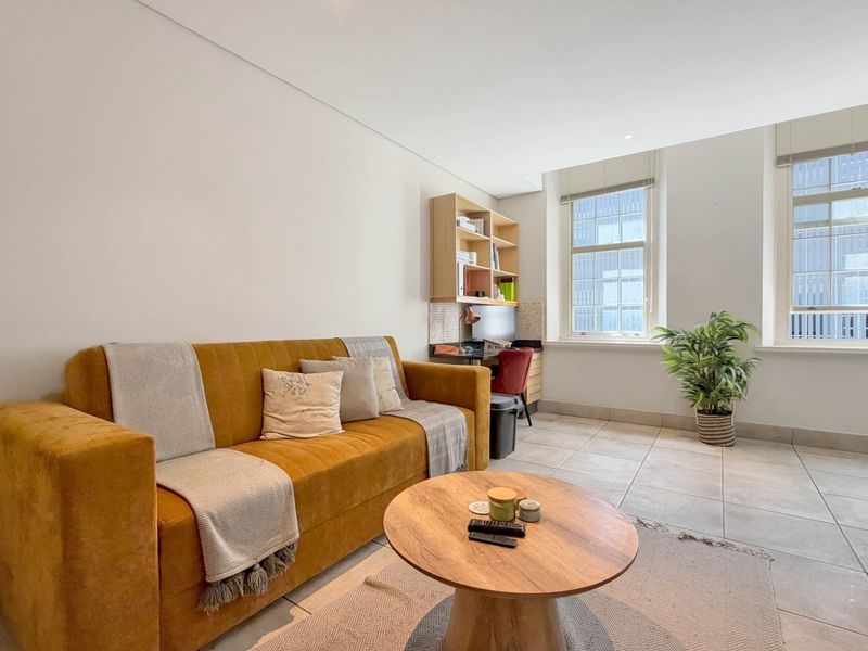 A bright living room featuring neutral tiled flooring, built-in shelving, and large sash windows that provide ample natural light.