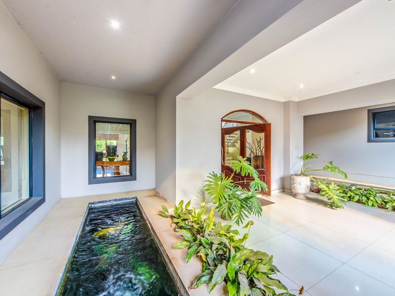 A spacious entrance hall featuring a built-in indoor water feature, large format floor tiles, and a grand wooden front door.