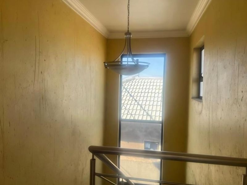 A staircase landing area featuring a pendant light fixture, metal railing, and windows, currently showing significant wear and scuffing on the wall surfaces.