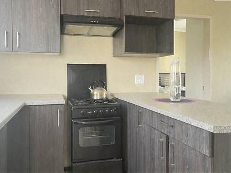A compact kitchen featuring dark wood-look cabinetry, stone-effect laminate countertops, a freestanding oven with extractor fan, and a neutral splashback.