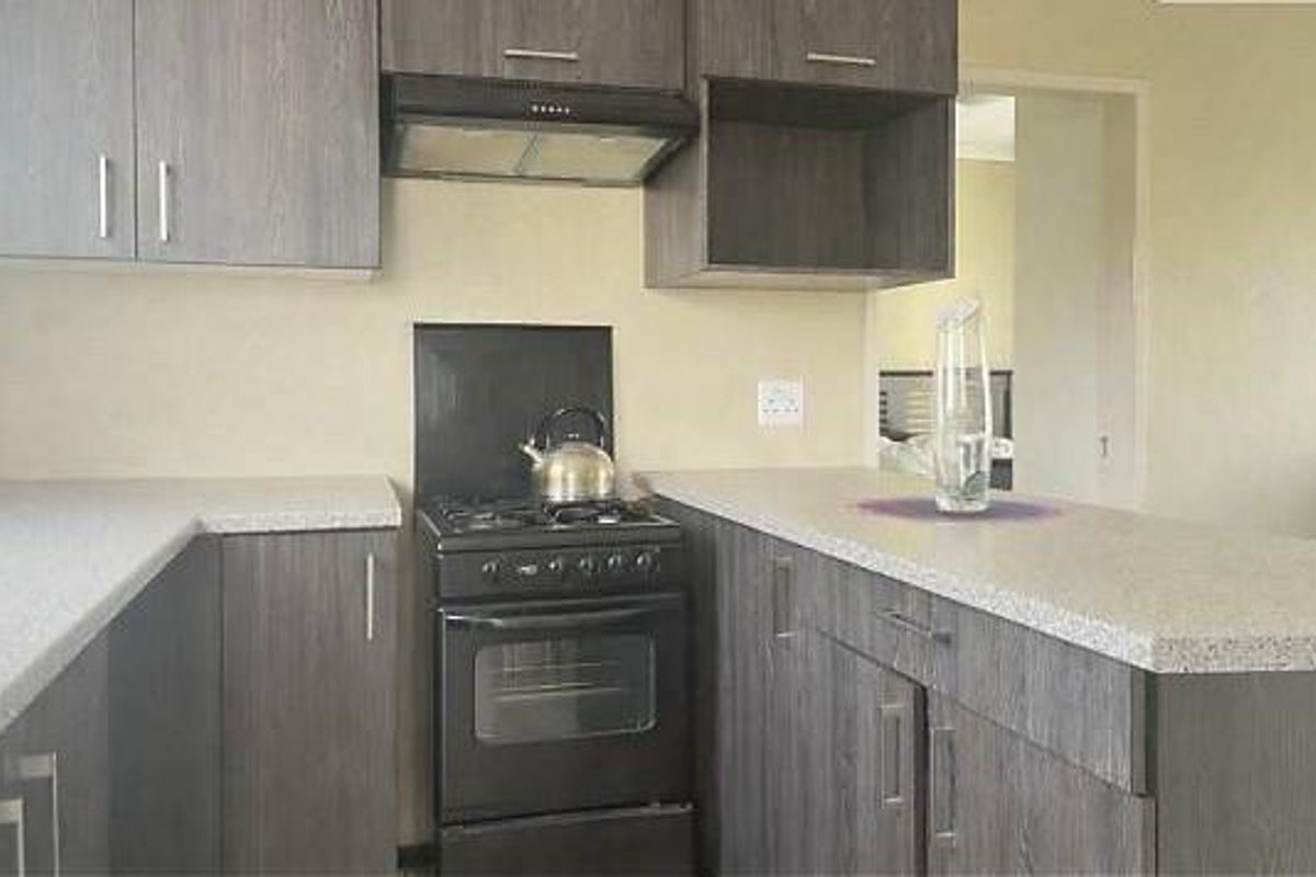 A compact kitchen featuring dark wood-look cabinetry, stone-effect laminate countertops, a freestanding oven with extractor fan, and a neutral splashback.