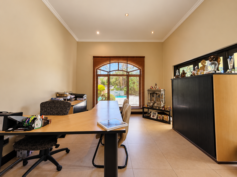 A spacious home office featuring tiled flooring, recessed lighting, and a large arched window providing a view of the outdoor pool area.