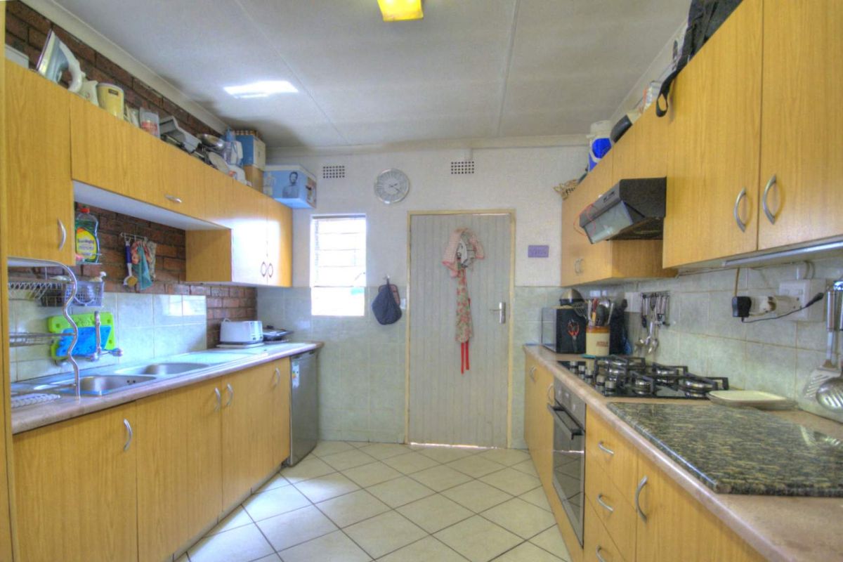 A functional galley-style kitchen featuring wood-look cabinetry, built-in gas hob, oven, extractor fan, and tiled flooring.