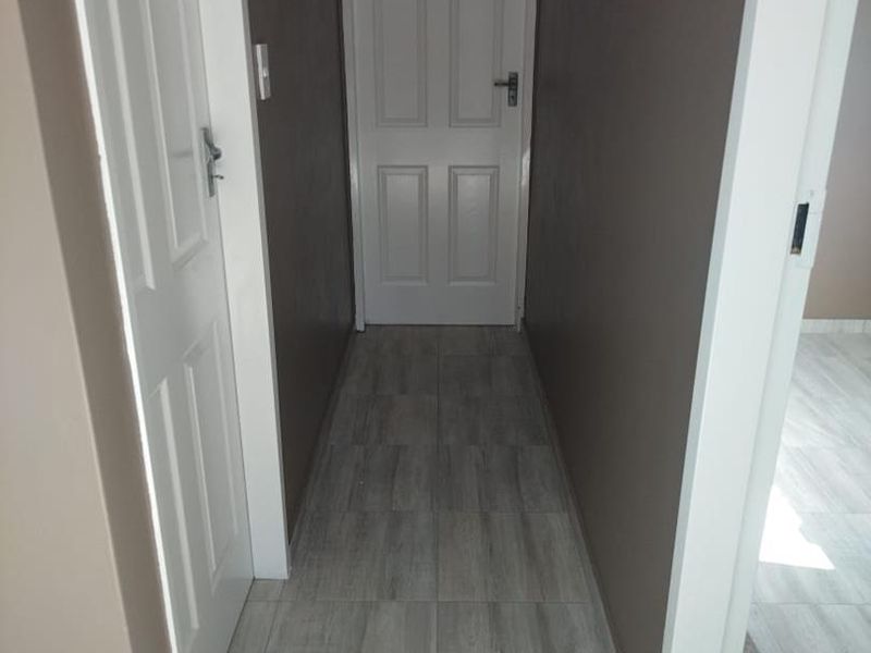A clean, empty hallway featuring modern grey wood-look floor tiles and dark painted walls, connecting multiple rooms within the home.