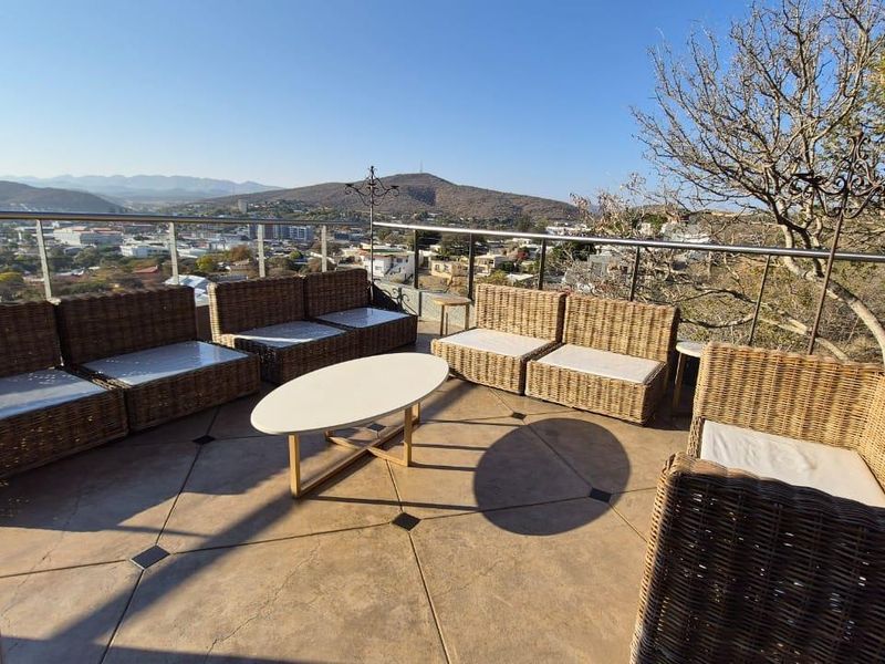 Spacious outdoor balcony featuring a glass balustrade and tiled flooring, offering expansive elevated views of the surrounding landscape and city.
