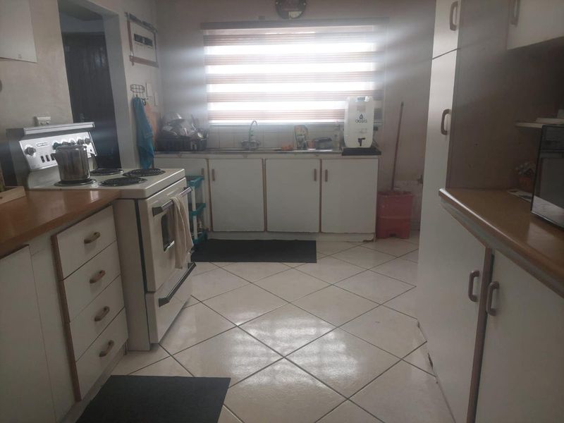 A functional kitchen featuring white cabinetry, laminate countertops, a freestanding stove, and tiled flooring, offering a practical layout with potential for modern updates.